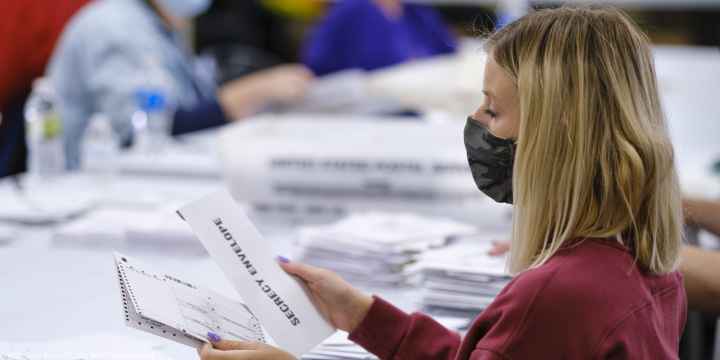 A woman with a surgical mask opening absentee ballots.